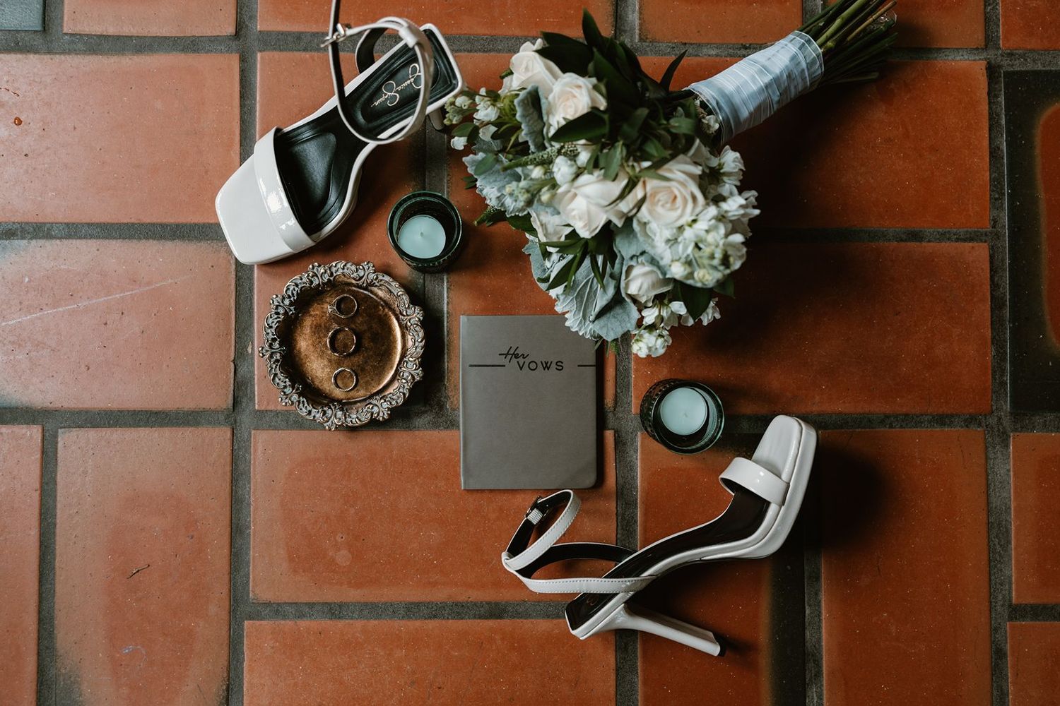 Wedding accessories including shoes, bouquet and rings arranged on terracotta tiles.