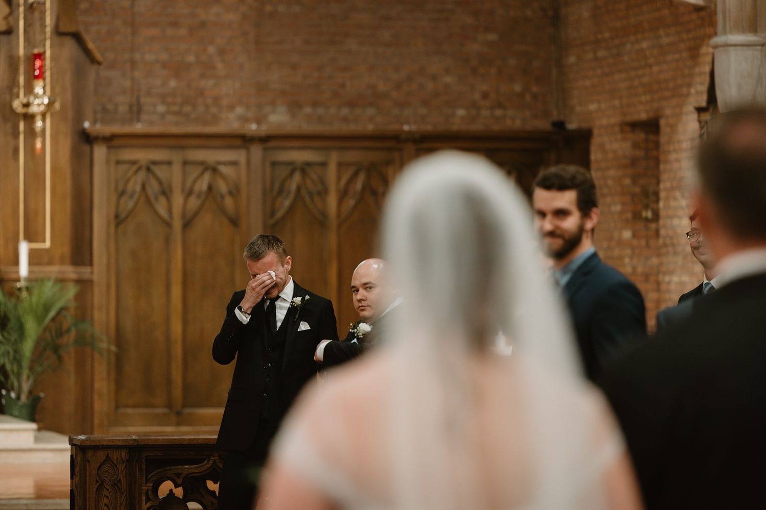Emotional catholic wedding photography moment of groom crying while. bride walks down the aisle.
