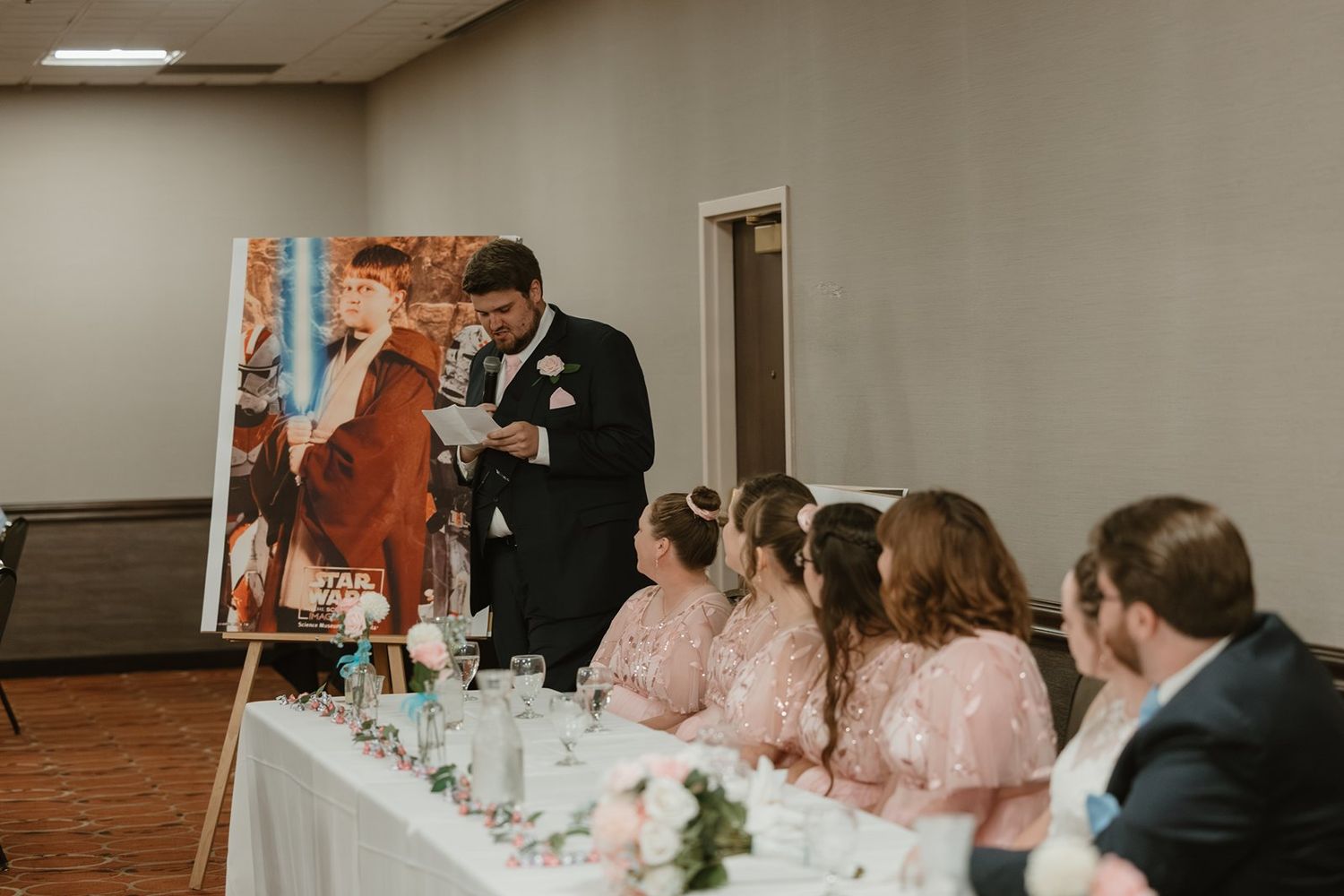 Wedding reception scene with guests in pink dresses and formal attire seated at decorated tables.
