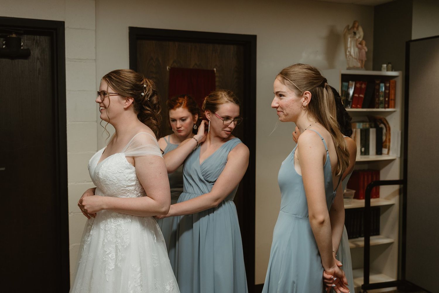 People stand in line wearing formal dresses in white and light blue colors during a wedding preparation.