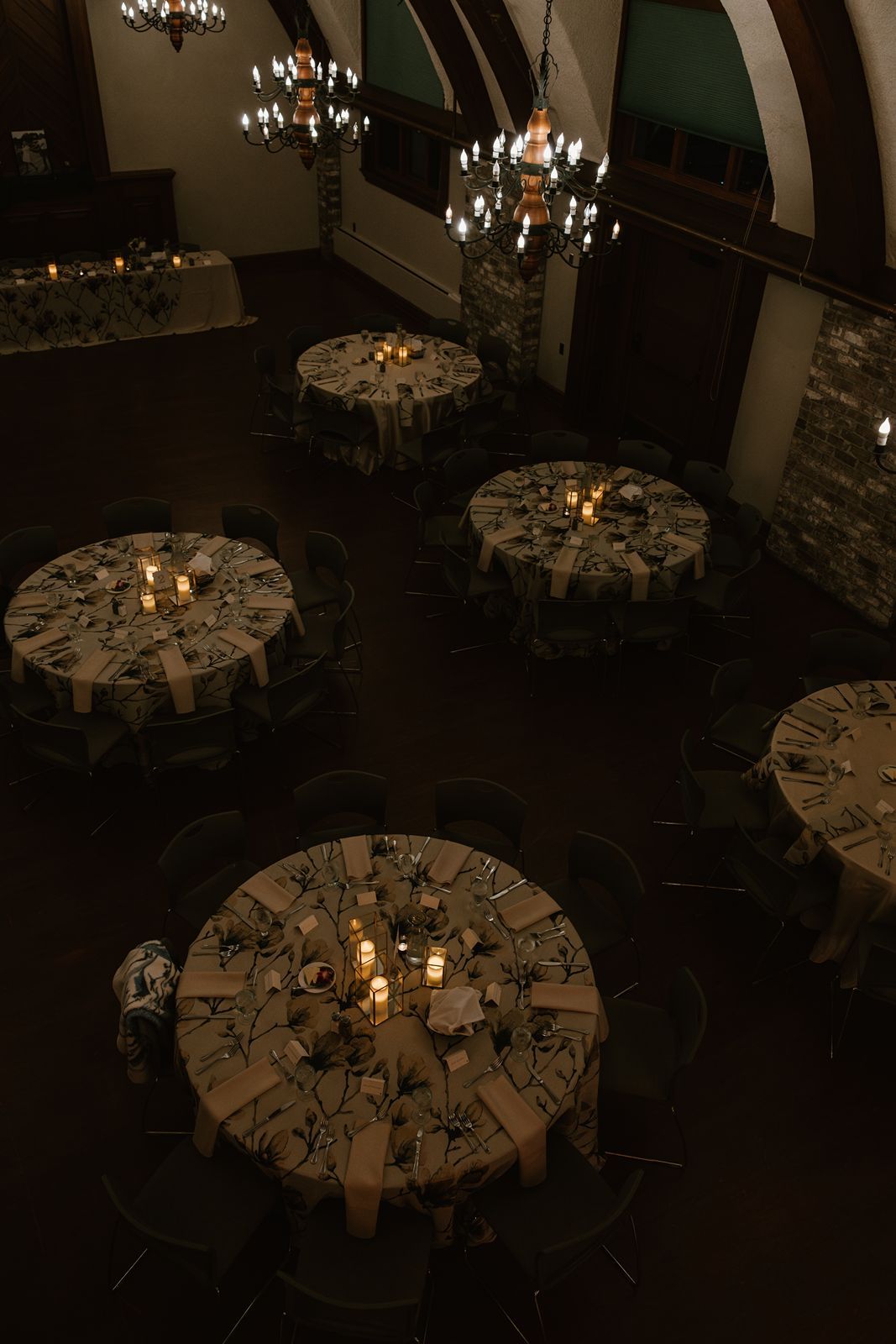 Elegant wedding reception setup with circular tables and chandeliers in a dimly lit venue.
