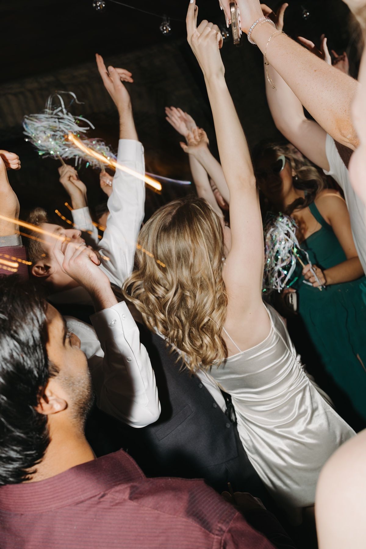 Guests dancing and celebrating at a lively wedding reception with raised arms and confetti streamers.