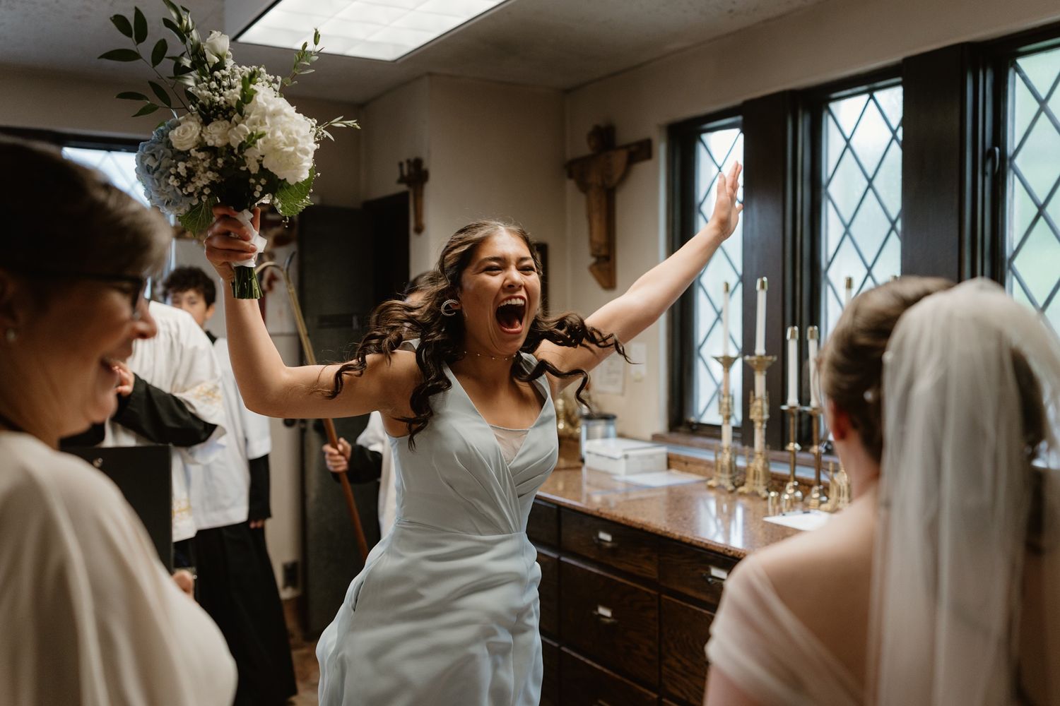 candid, joyful moment between a bride and a bridesmaid after a Catholic wedding mass