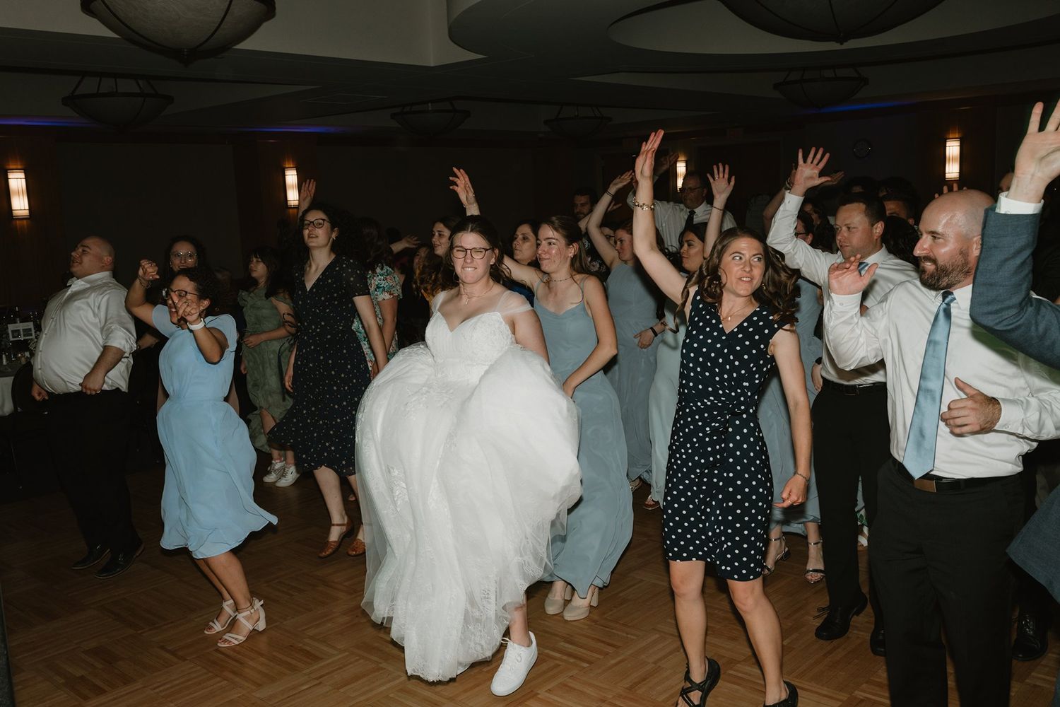 People dancing and enjoying themselves on a dimly lit dance floor at a wedding celebration.