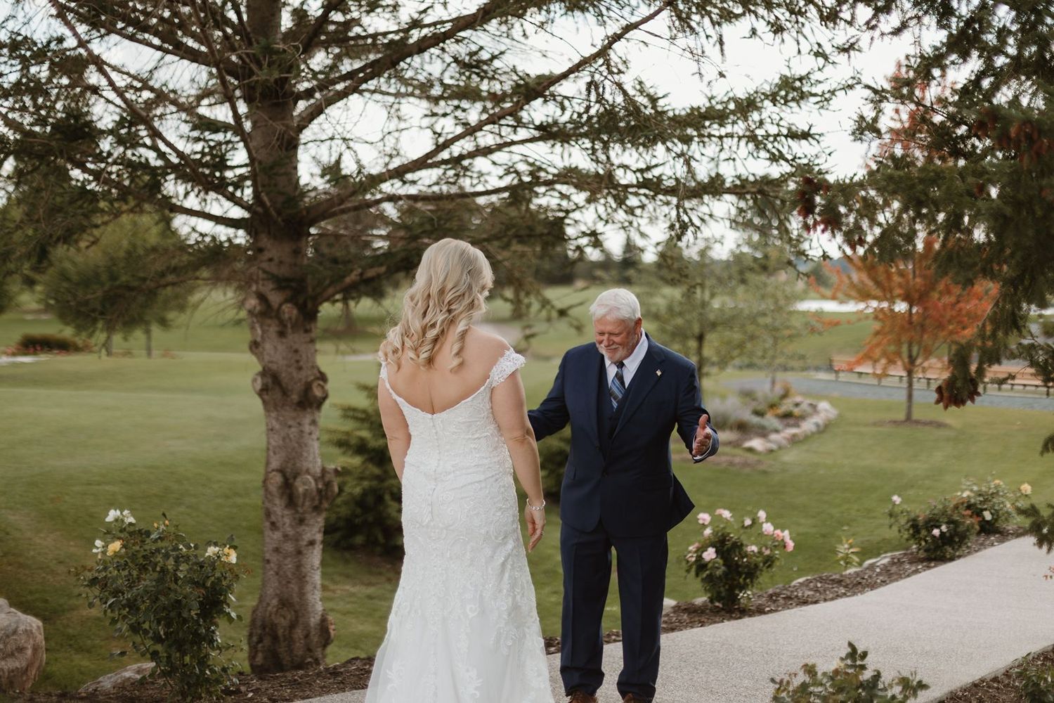 A heartwarming moment between a bride in white dress and elderly escort walking along a garden path.