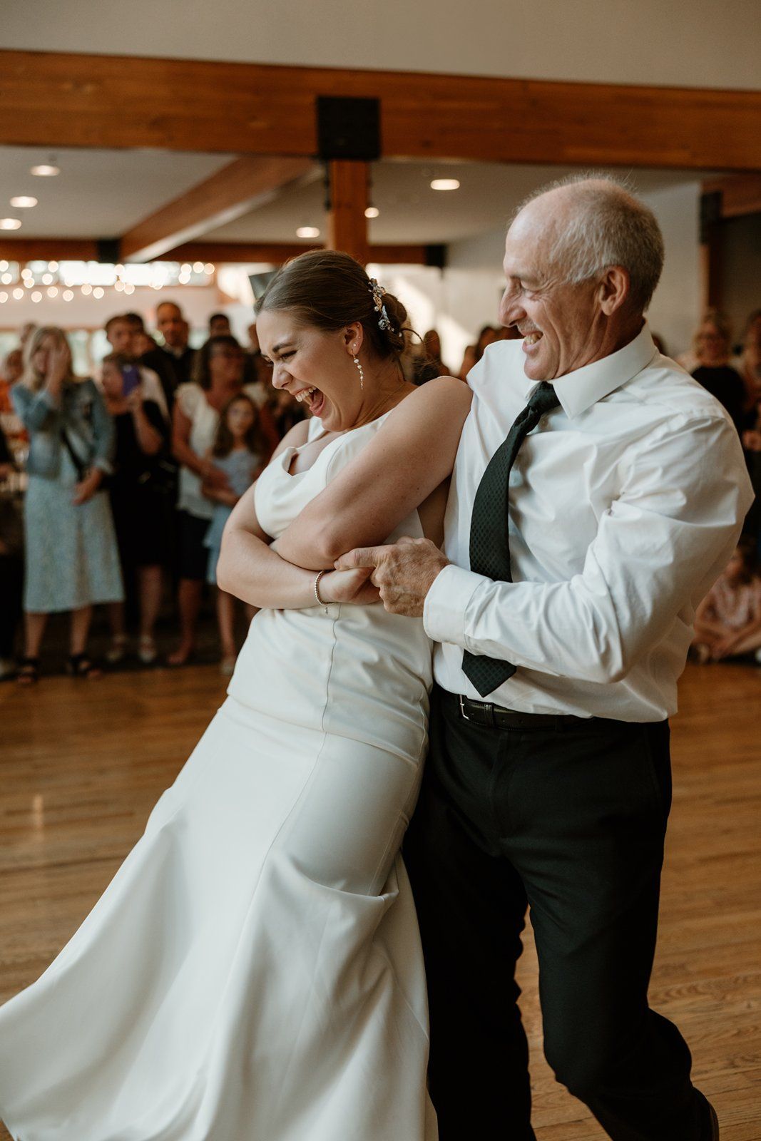 A joyful moment on the dance floor at a wedding reception as a bride dances with an older guest in formal attire.