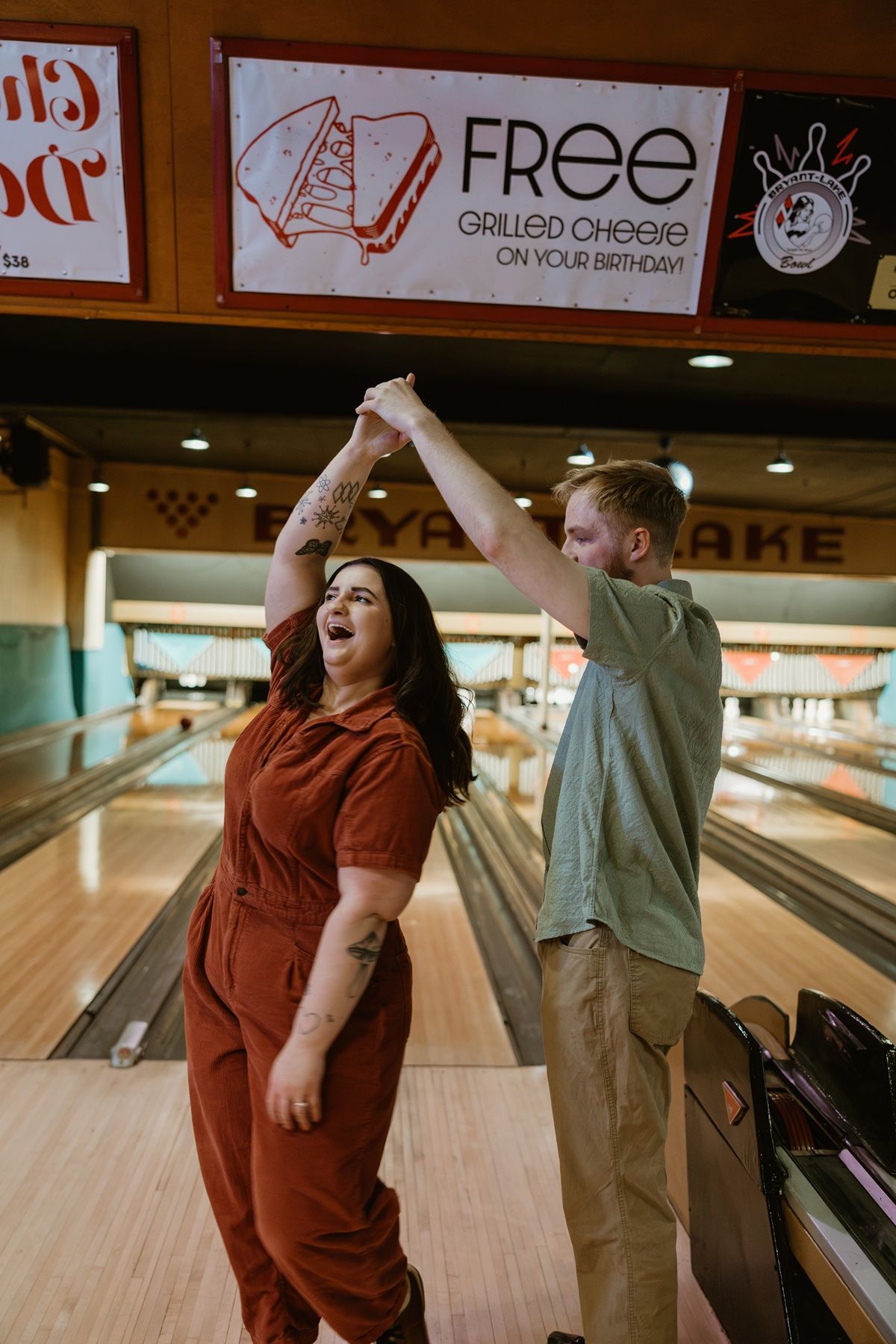 Two people celebrate and cheer while bowling at a retro-style bowling alley with wooden lanes.