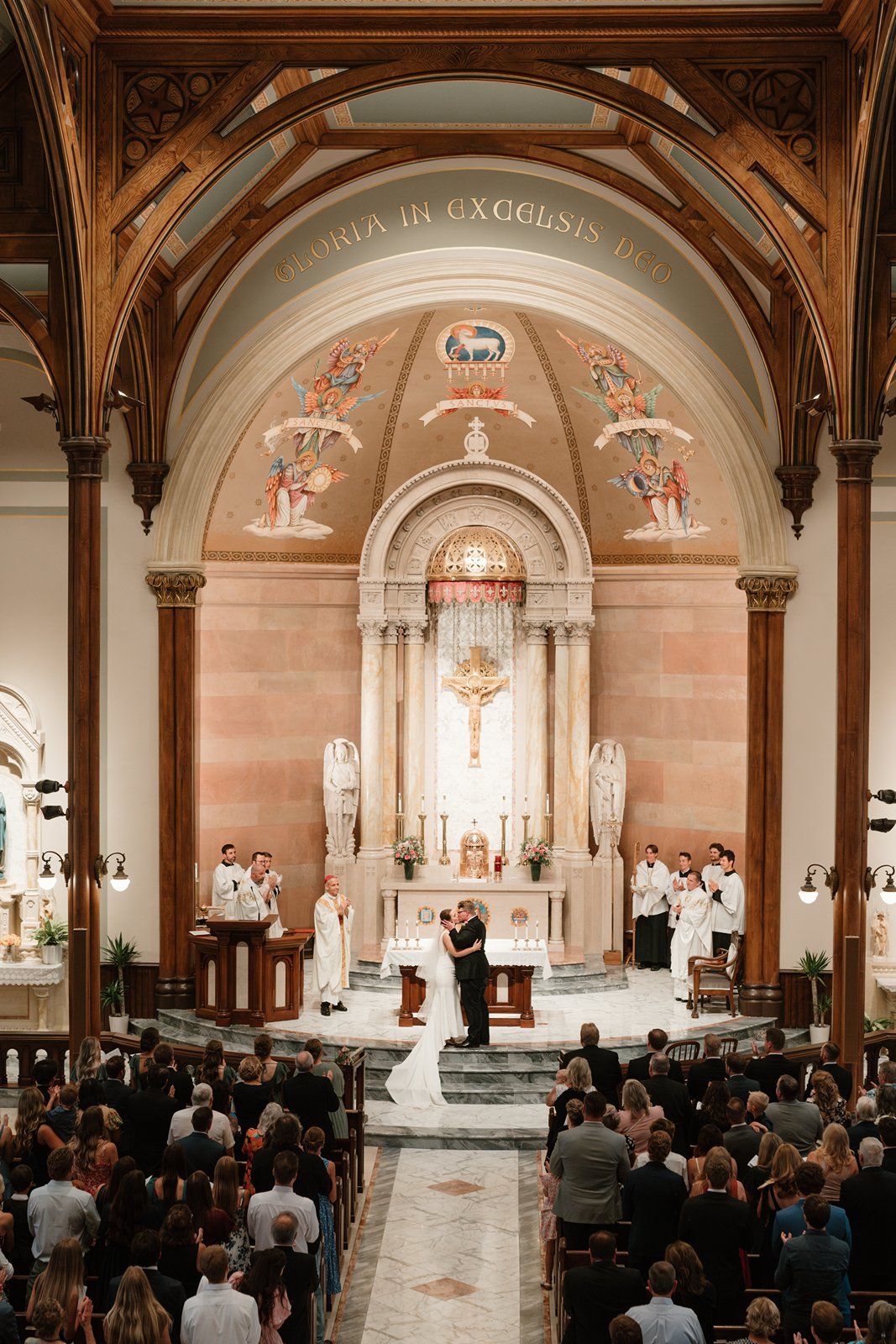 Panoramic view of Catholic church wedding ceremony with guests seated in traditional wooden pews.