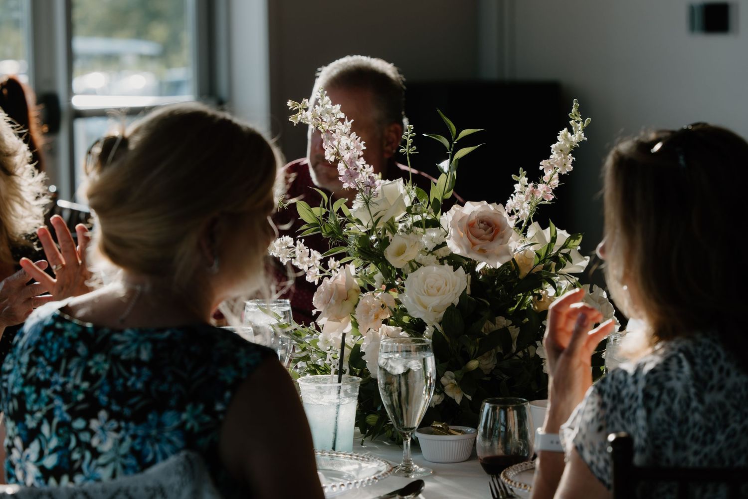 Floral centerpiece with pink and white flowers on a table surrounded by guests at a gathering.