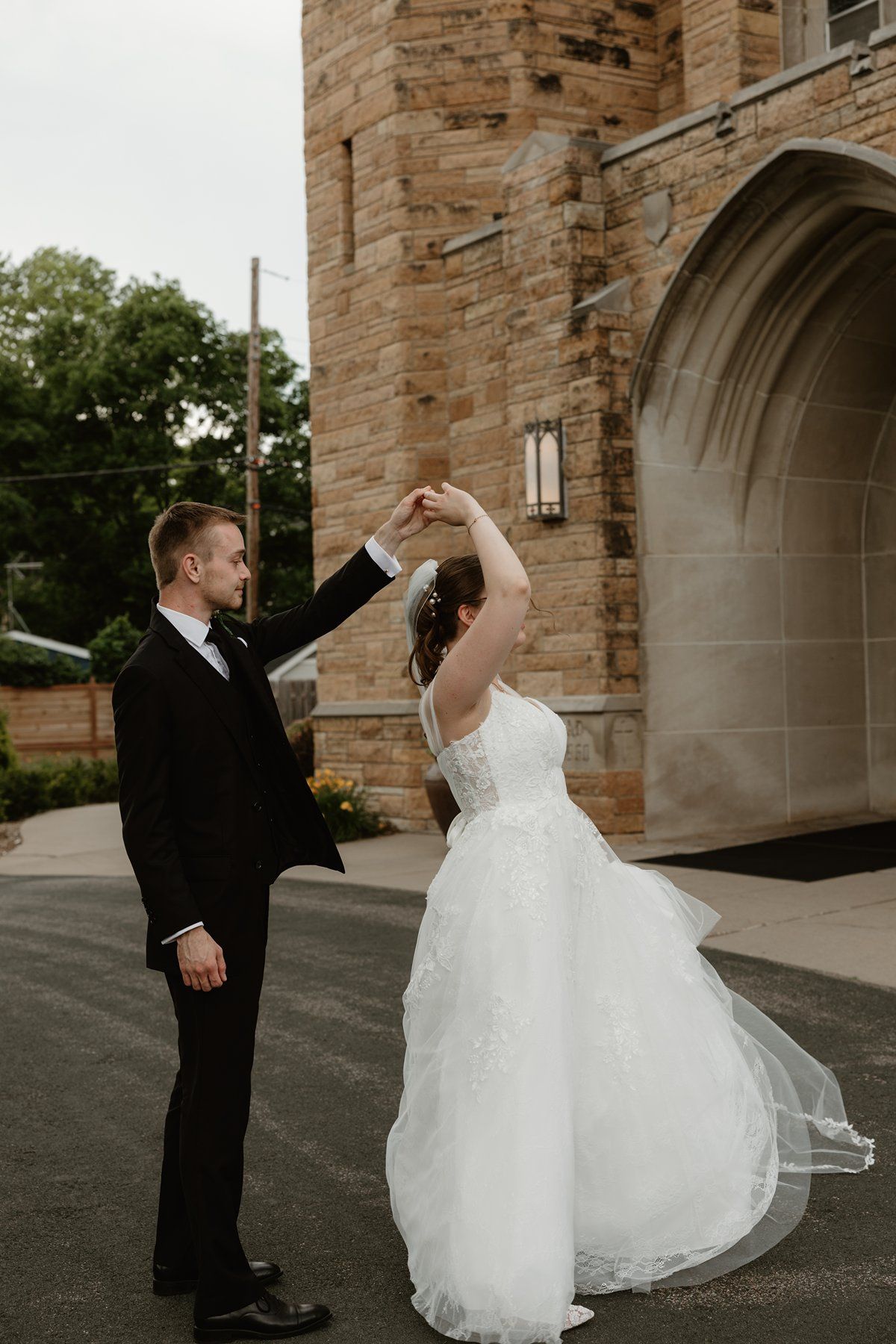 A couple dances and twirls outside a stone church building during their wedding celebration.