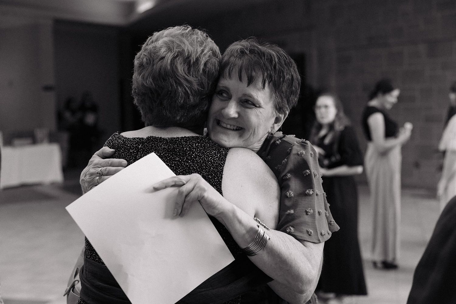 Black and white photo of wedding guests embracing at reception.