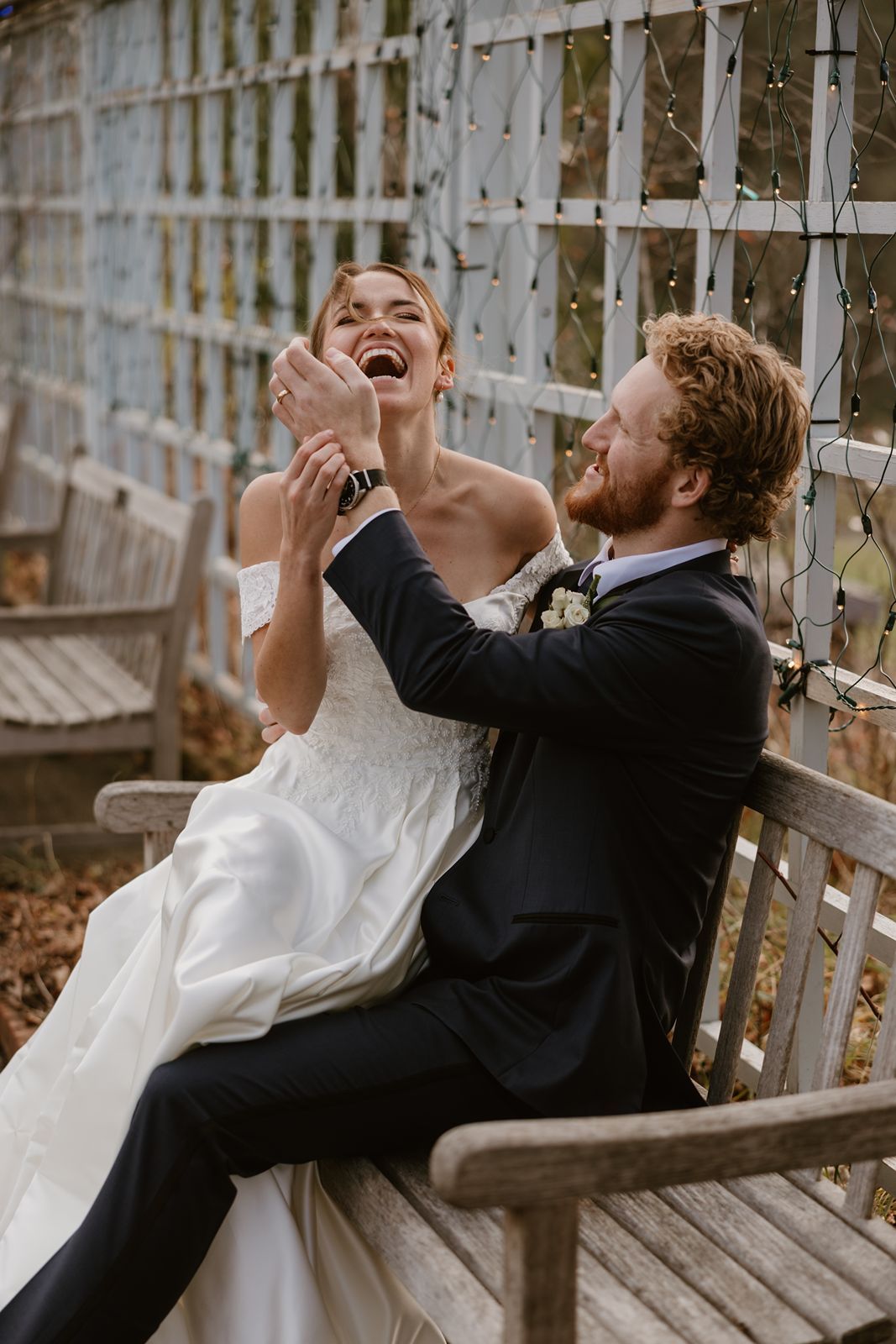Joyful wedding couple sharing a candid laughing moment on wooden bench.