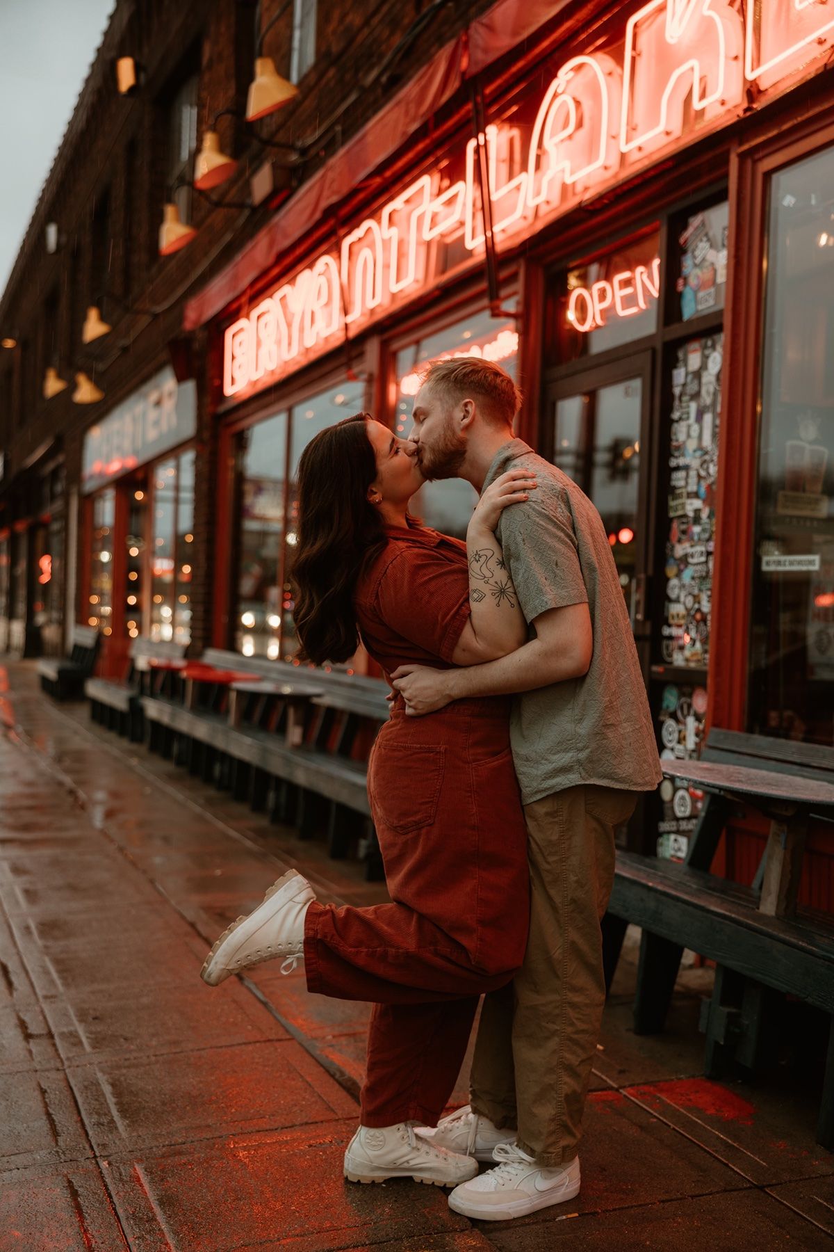 A couple shares an intimate moment outside a bar with neon red lighting in the evening.