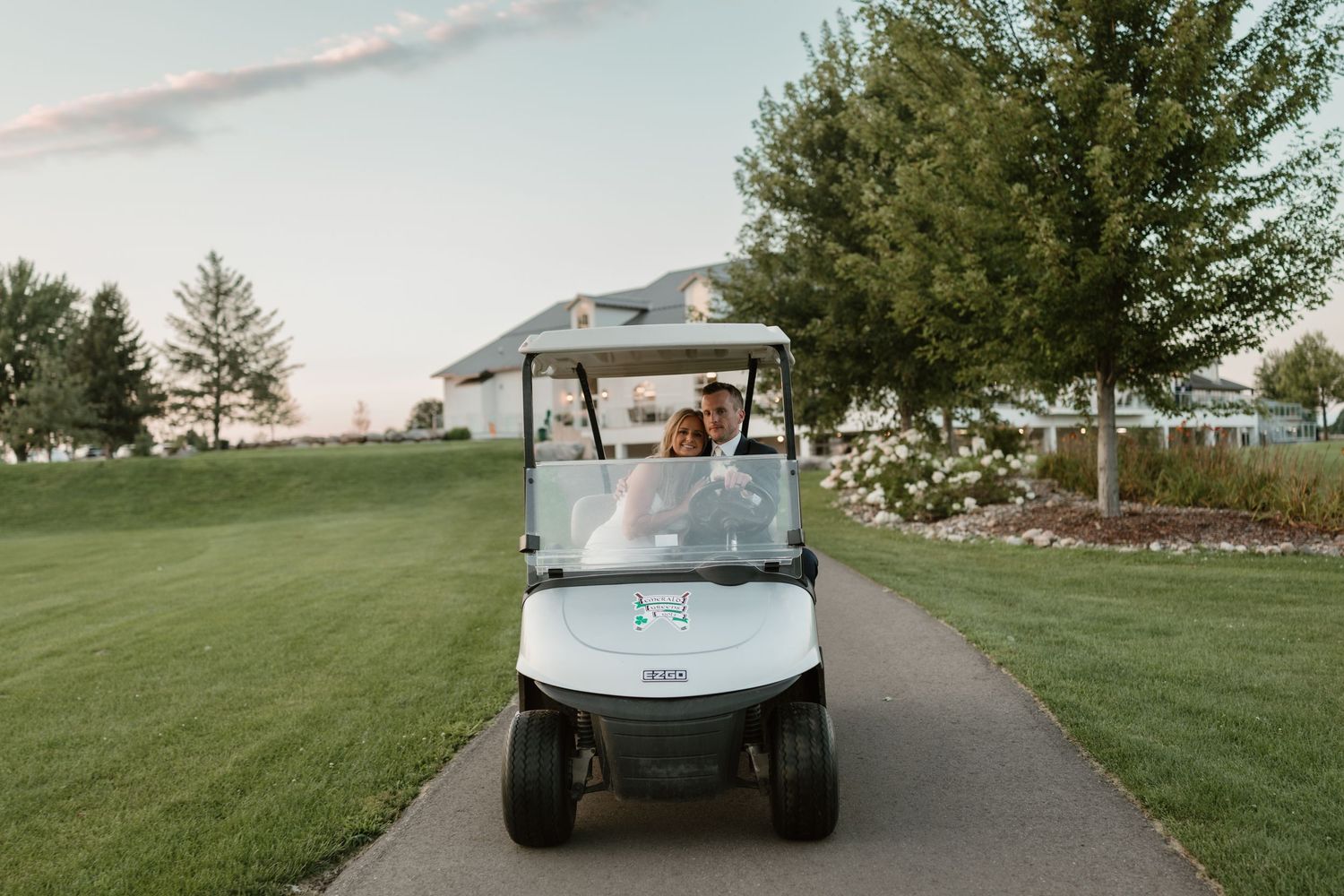 A golf cart driving on a paved path through a grassy area at sunset.
