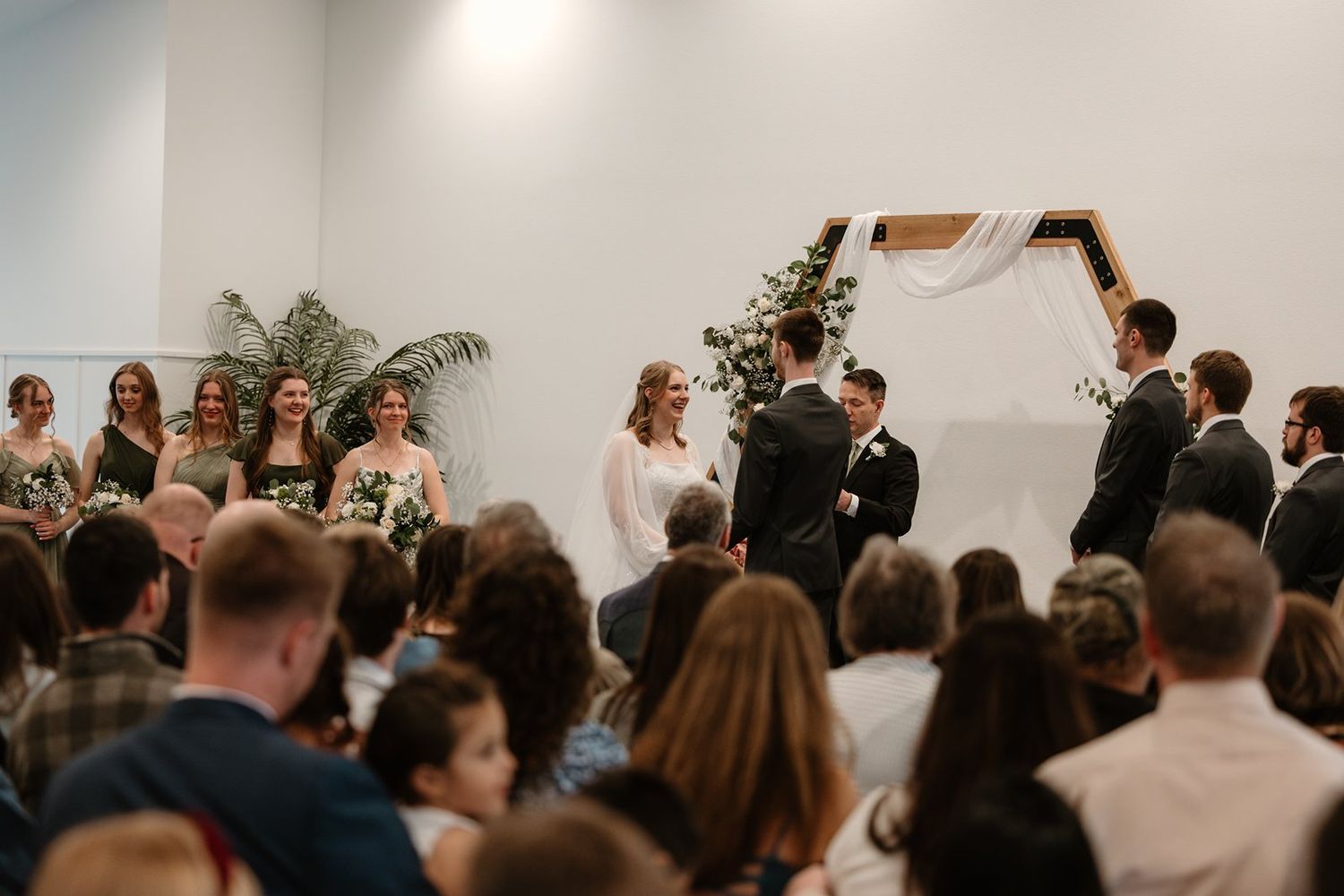Wedding guests stand together in a bright white room during an indoor ceremony celebration at The Pines Black