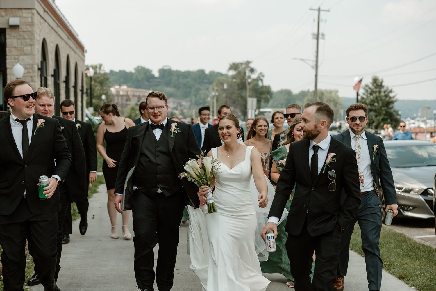 Wedding party walks together and laughs while strolling along a waterfront path on their celebration day.