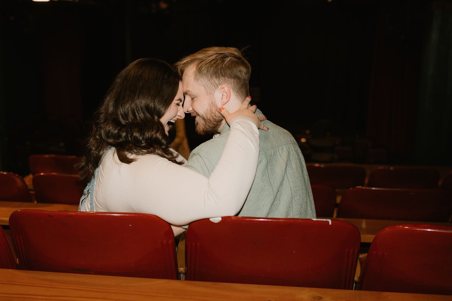 Two people share a romantic moment in the red velvet seats of an empty theater.