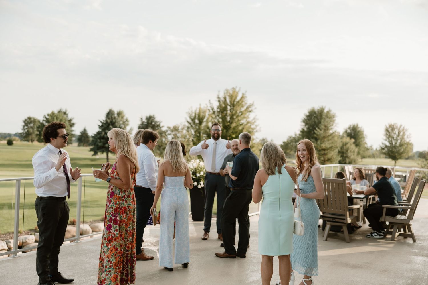 Guests gather outdoors at a scenic wedding venue with tables and chairs set up on a patio area.