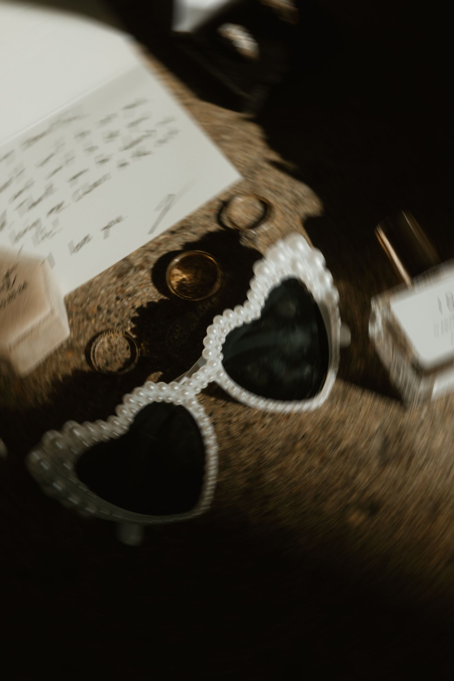 Vintage-style heart-shaped sunglasses with white beaded frames rest on an open book in moody lighting.