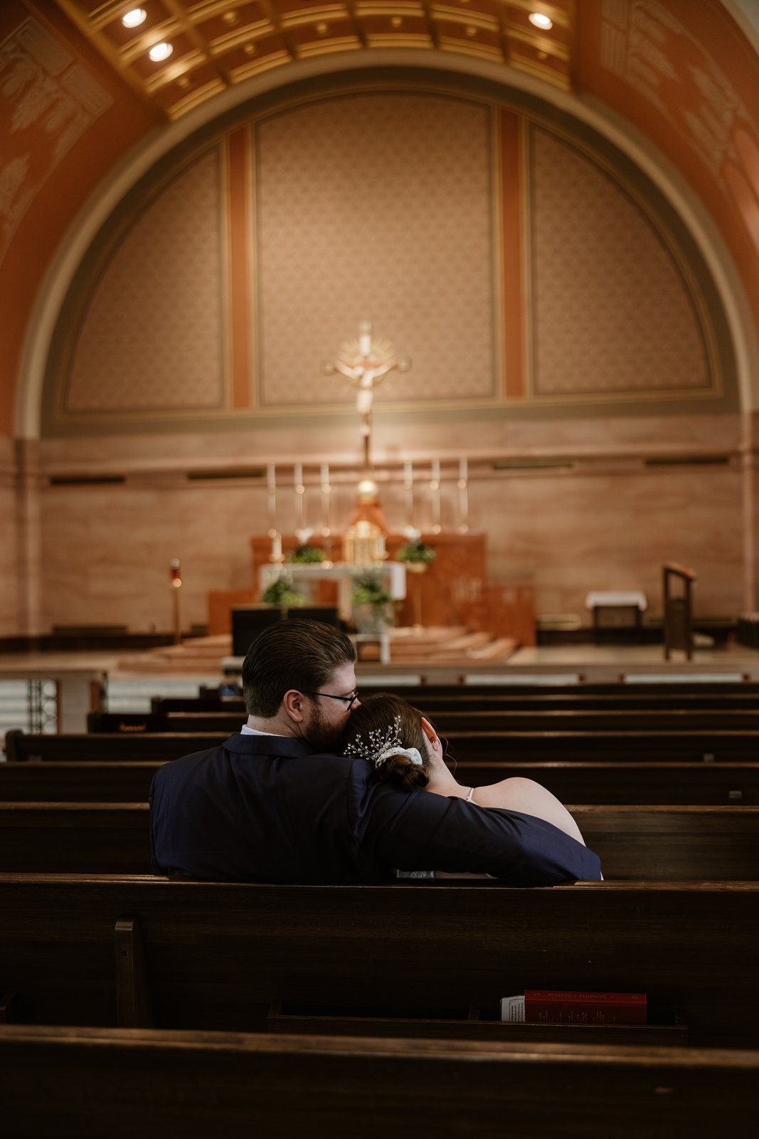 Inside a dimly lit church sanctuary with wooden pews and arched ceilings during an intimate moment of prayer.