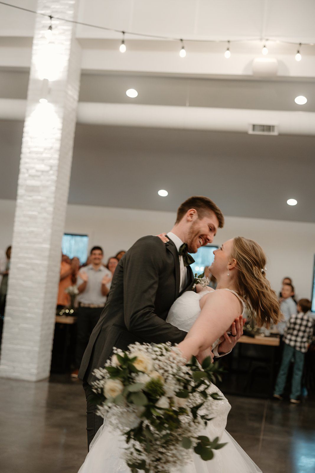 A romantic dip kiss between newlyweds during their first dance in a modern white-columned reception venue.