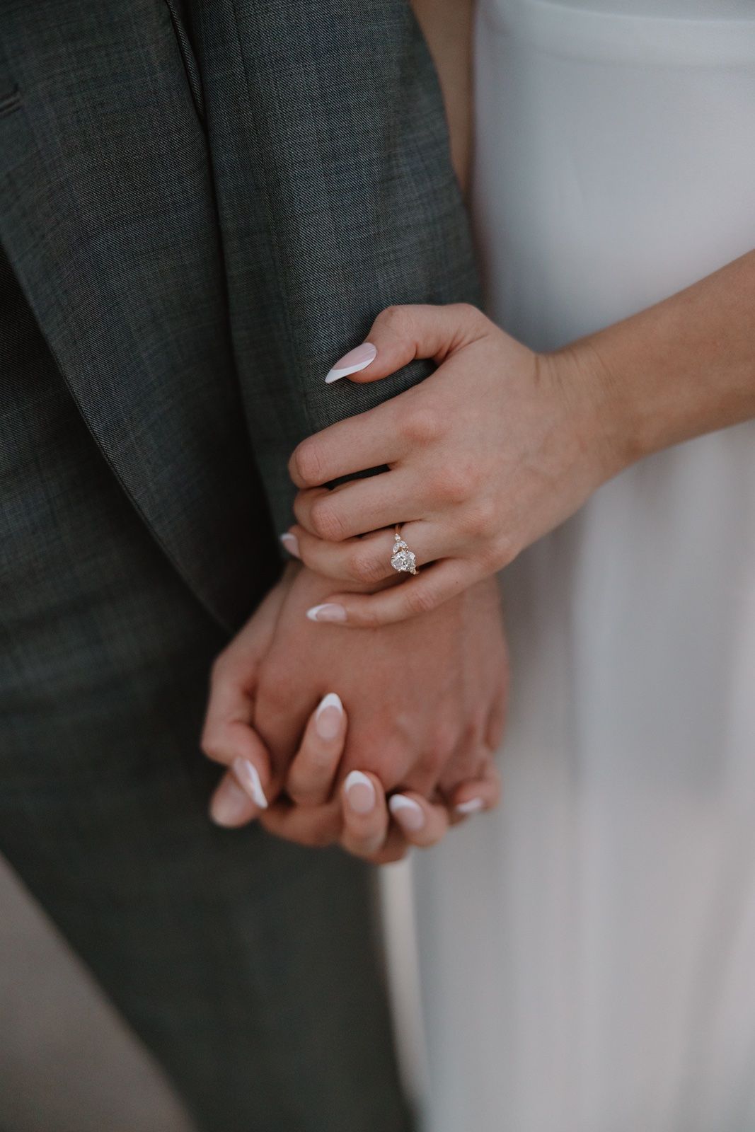 Bride and groom holding hands, showcasing a stunning diamond engagement ring on the bride's finger.