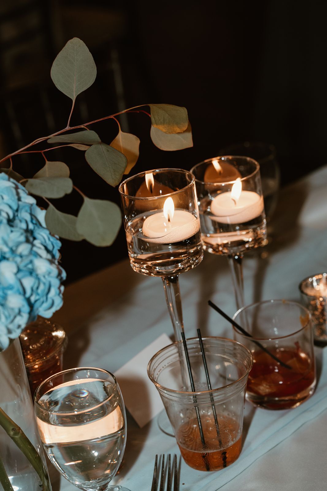 Romantic table setting with floating candles in stemware and eucalyptus leaves for a wedding.
