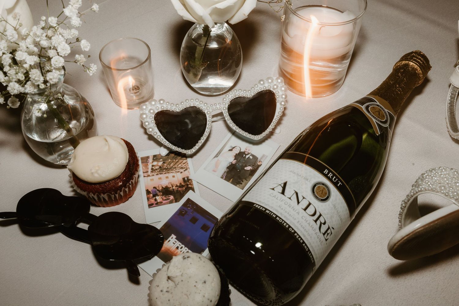 Romantic table setting with heart plates, Asti wine bottle, lit candles and baby's breath flowers on white surface.