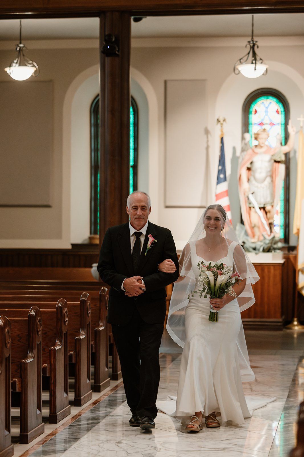 A wedding ceremony procession taking place in a church with stained glass windows and wooden pews.