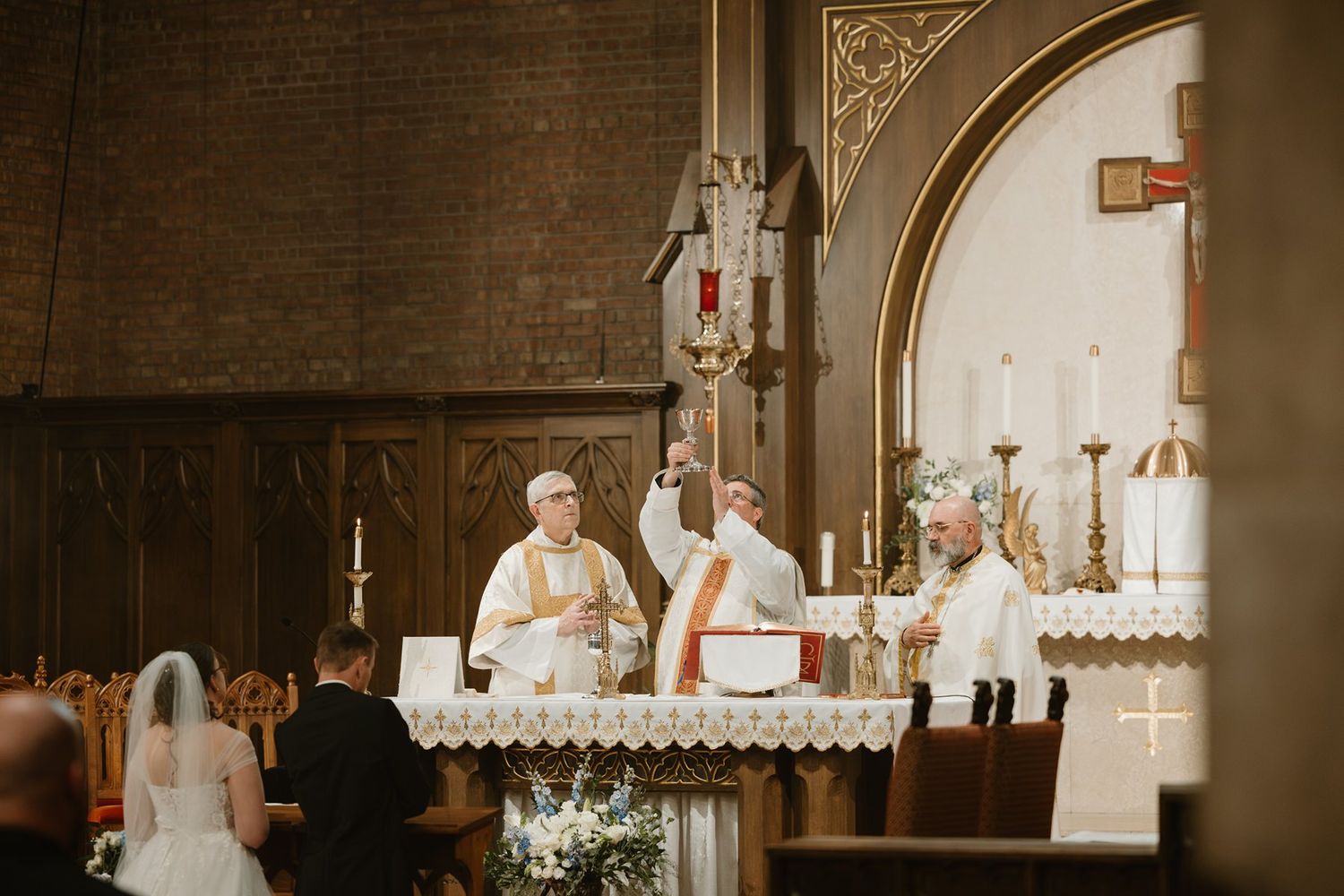 Catholic religious ceremony taking place at the altar of a traditional brick church sanctuary.
