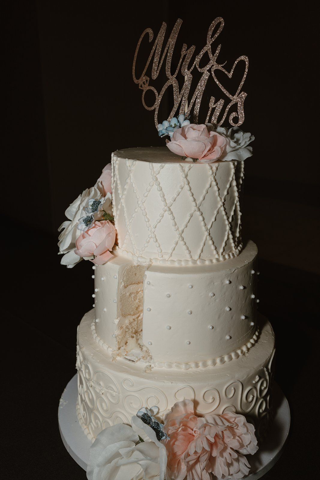 Elegant white wedding cake with diamond pattern, pearl accents, and delicate pink and blue floral decorations.