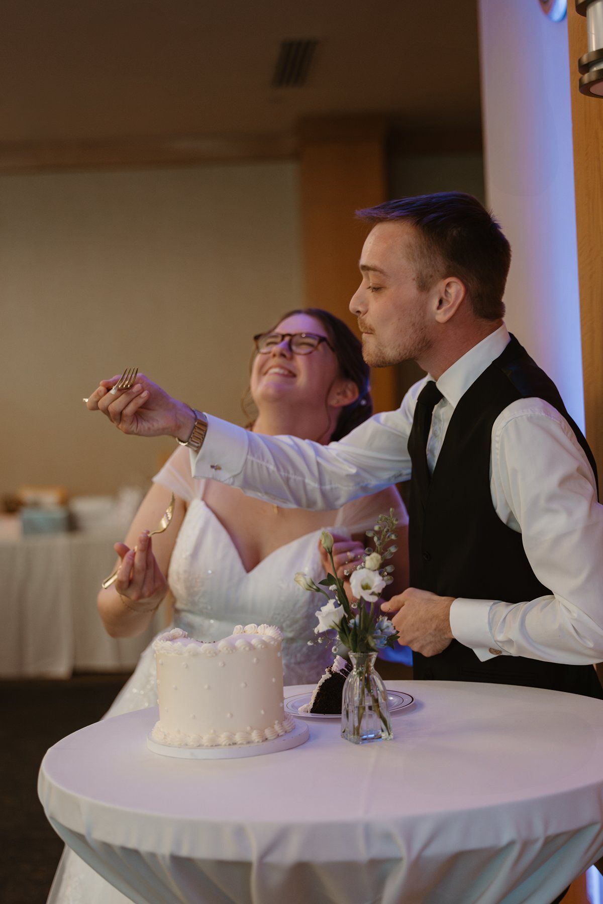 Newlyweds share a joyful moment while cutting their white wedding cake at their reception.