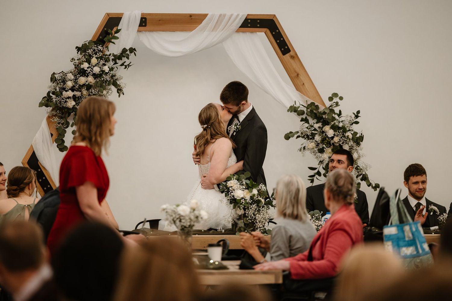 Wedding guests seated at long tables in an elegant reception hall with string lights overhead.