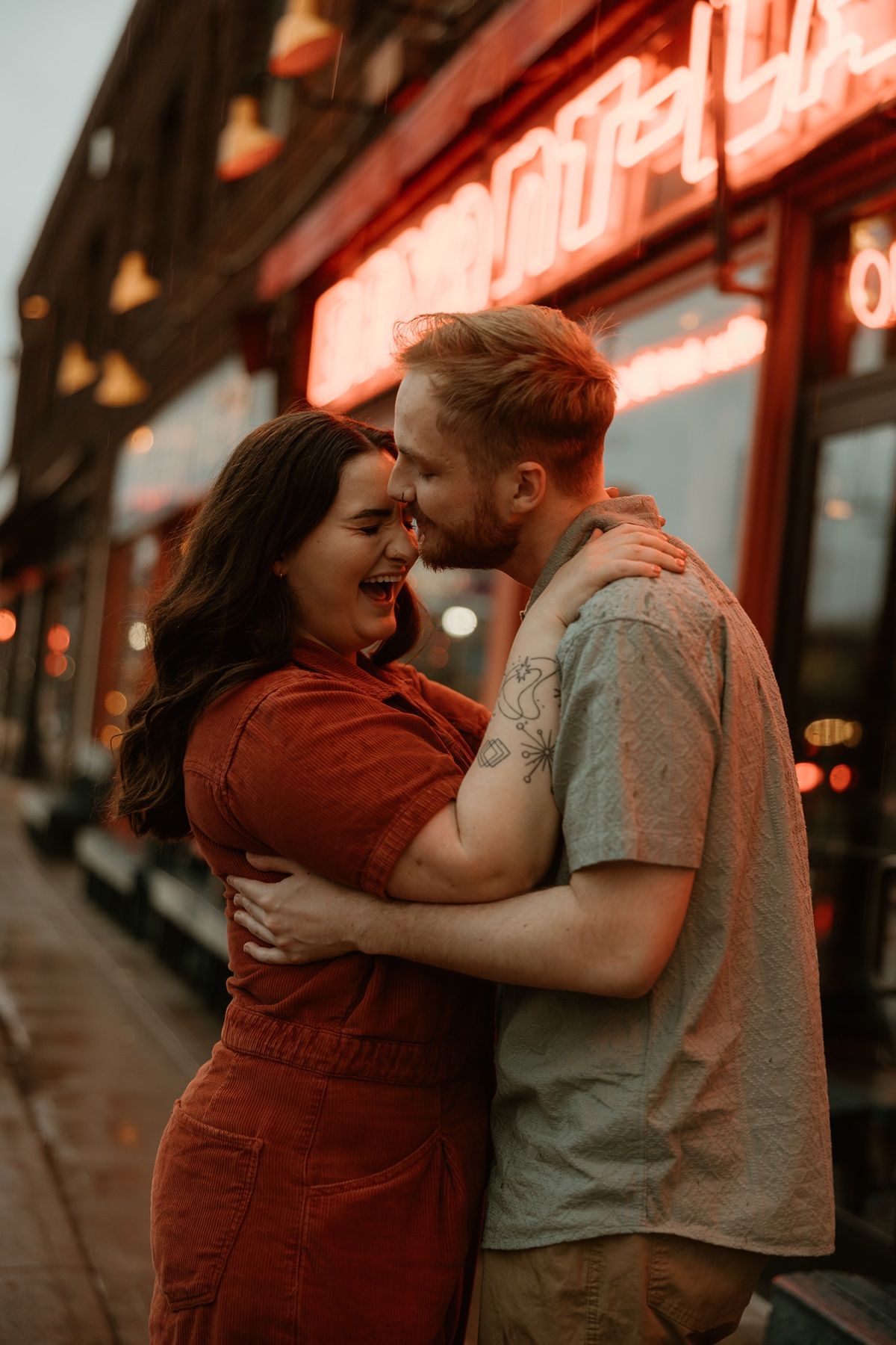 A tender embrace shared under warm neon lights during sunset outside a building.