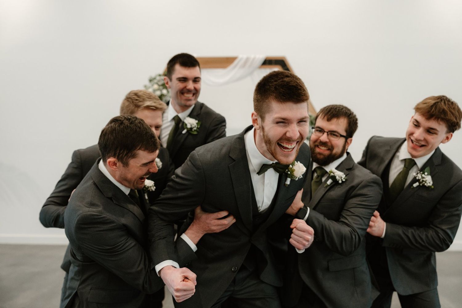 Group of groomsmen laugh and share a candid moment during wedding photos in black suits.