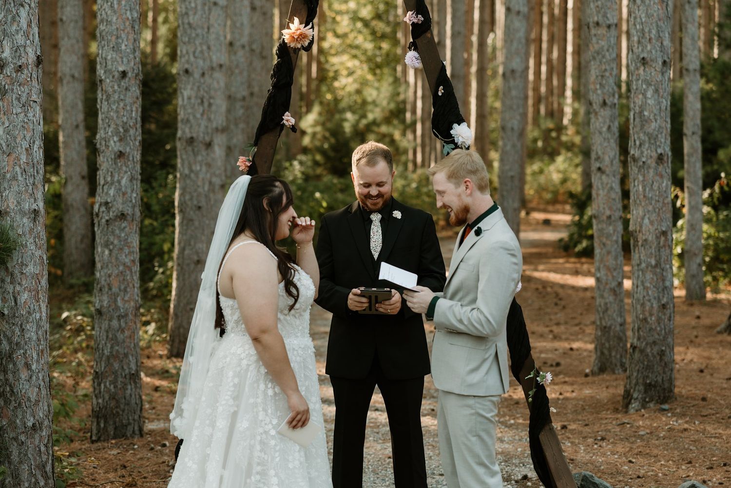 Couple exchanging vows with officiant in a sunlit pine forest wedding ceremony at Pinewood Weddings and Events.