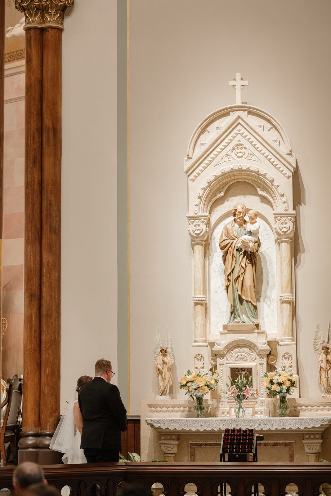 Wedding ceremony taking place in a traditional Catholic church with elegant white marble altar and religious statues.