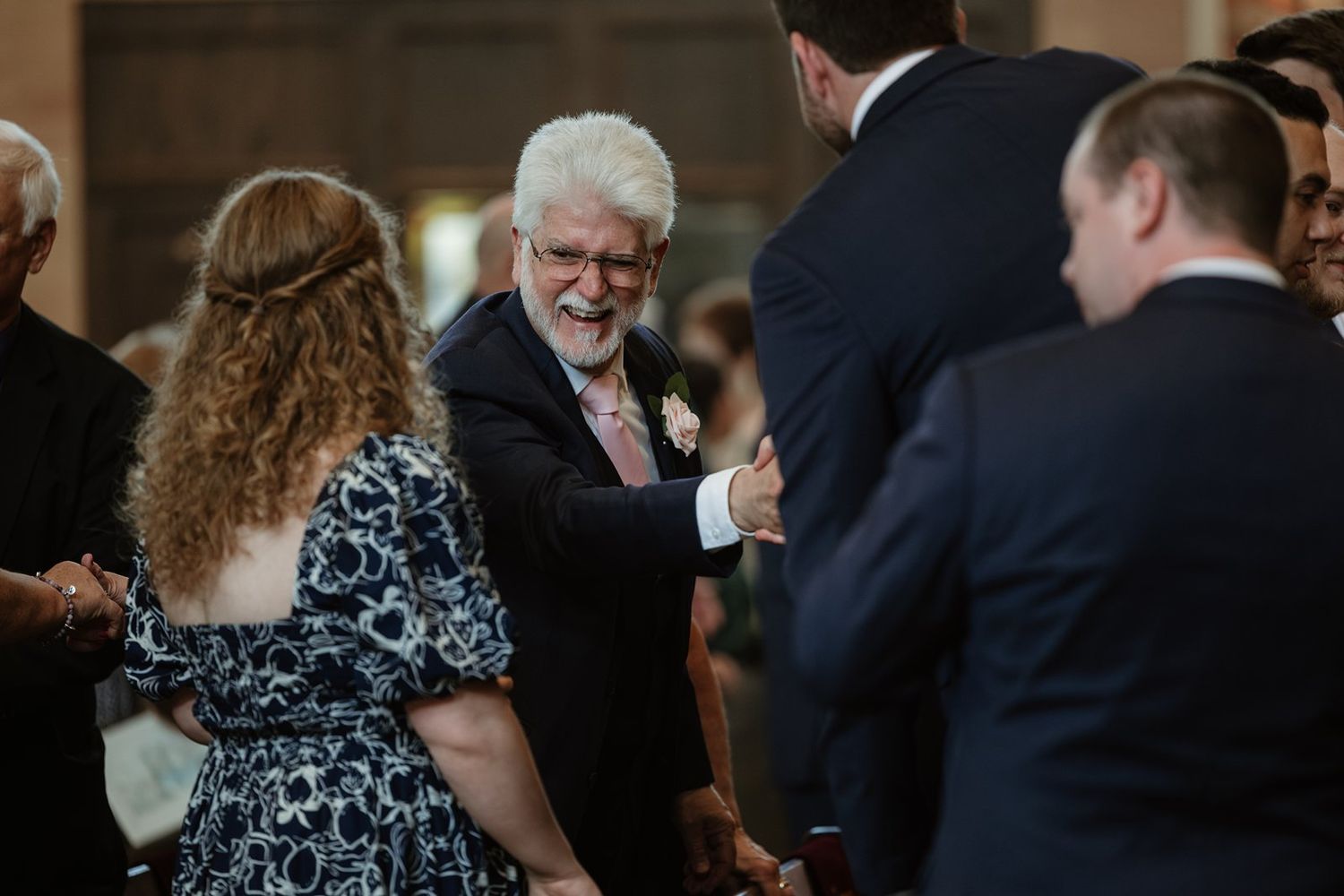 Wedding attendees gather in a church aisle between wooden pews during a celebration.