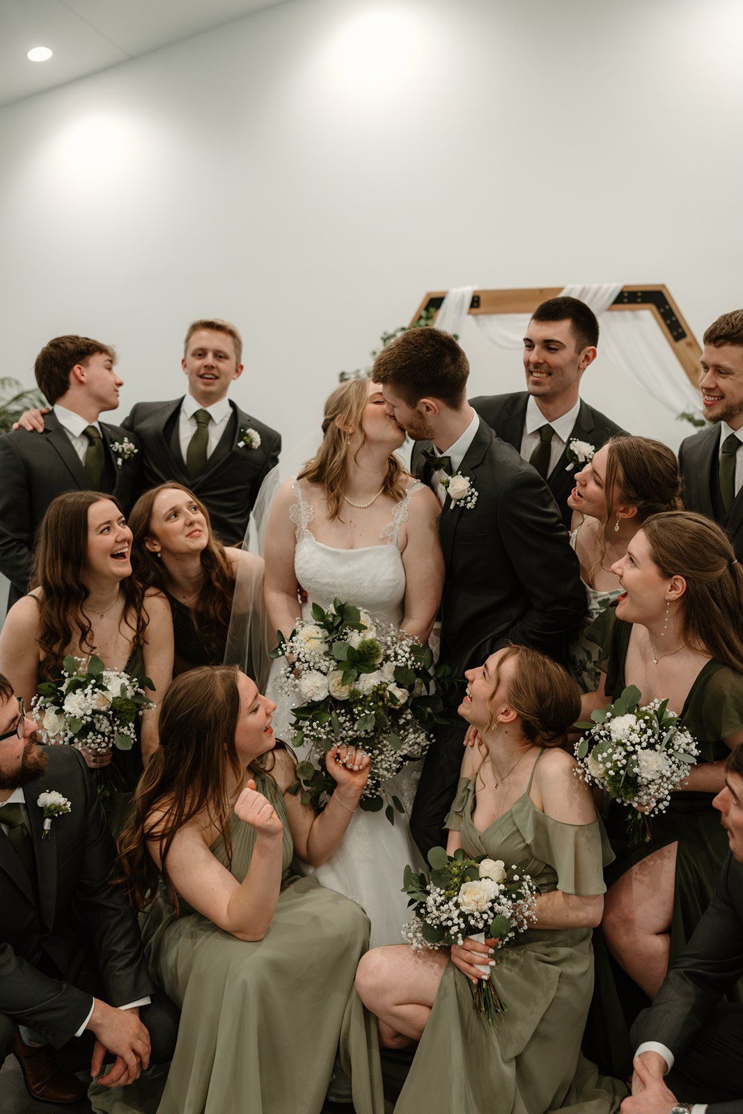 Wedding party members laugh together while holding white floral bouquets in a candid moment.