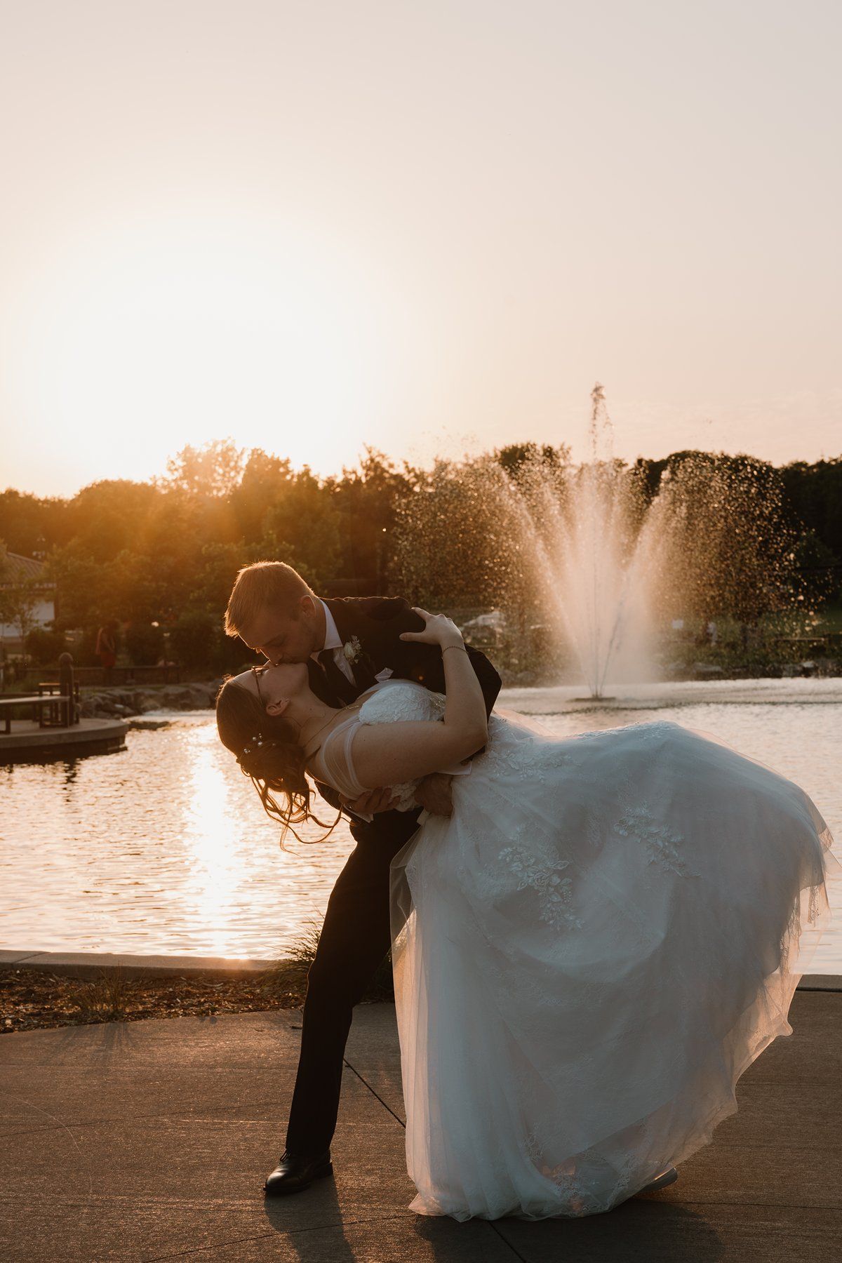 A dramatic dip pose during a sunset wedding dance, with a fountain and golden light creating a romantic backdrop.