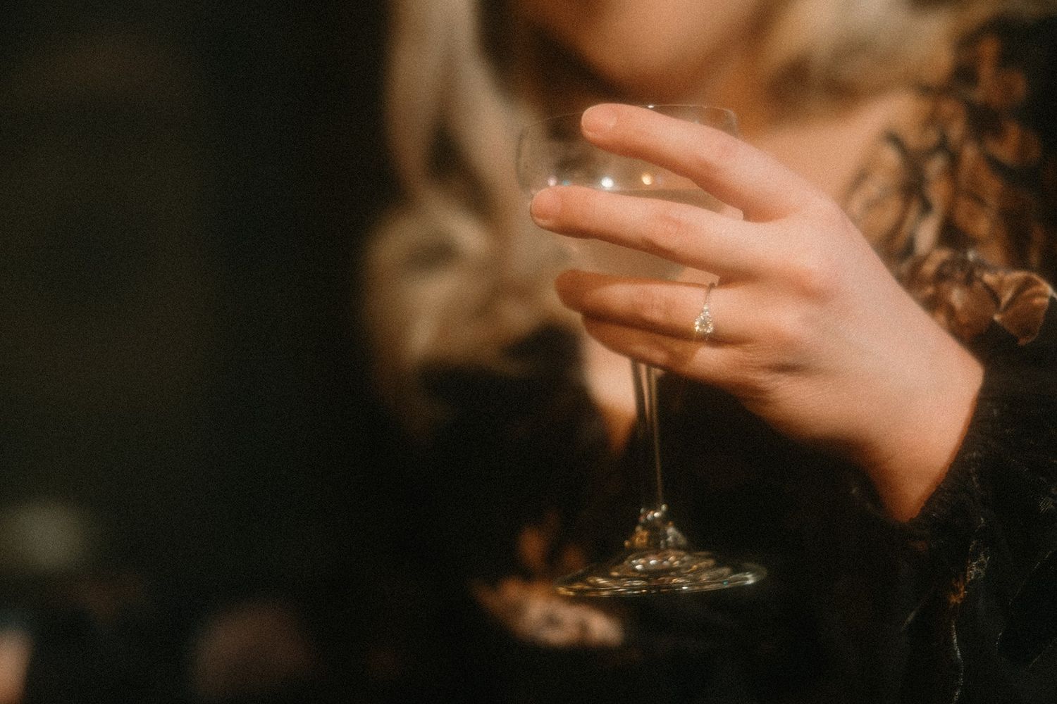 Hand holding a wine glass in dim lighting while wearing an elegant lace sleeve.
