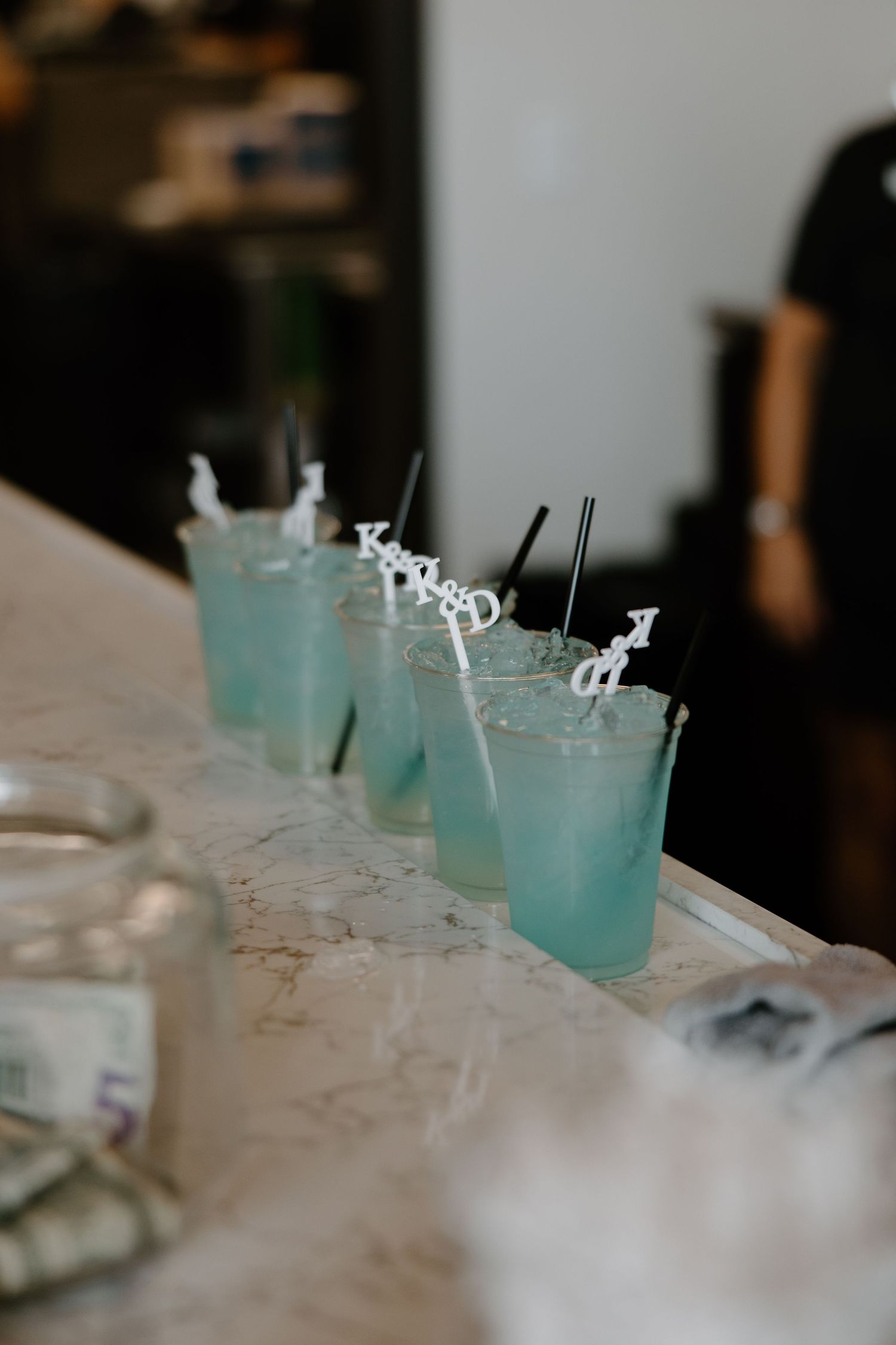 A row of light blue cocktails with salted rims and black straws served on a white marble counter.