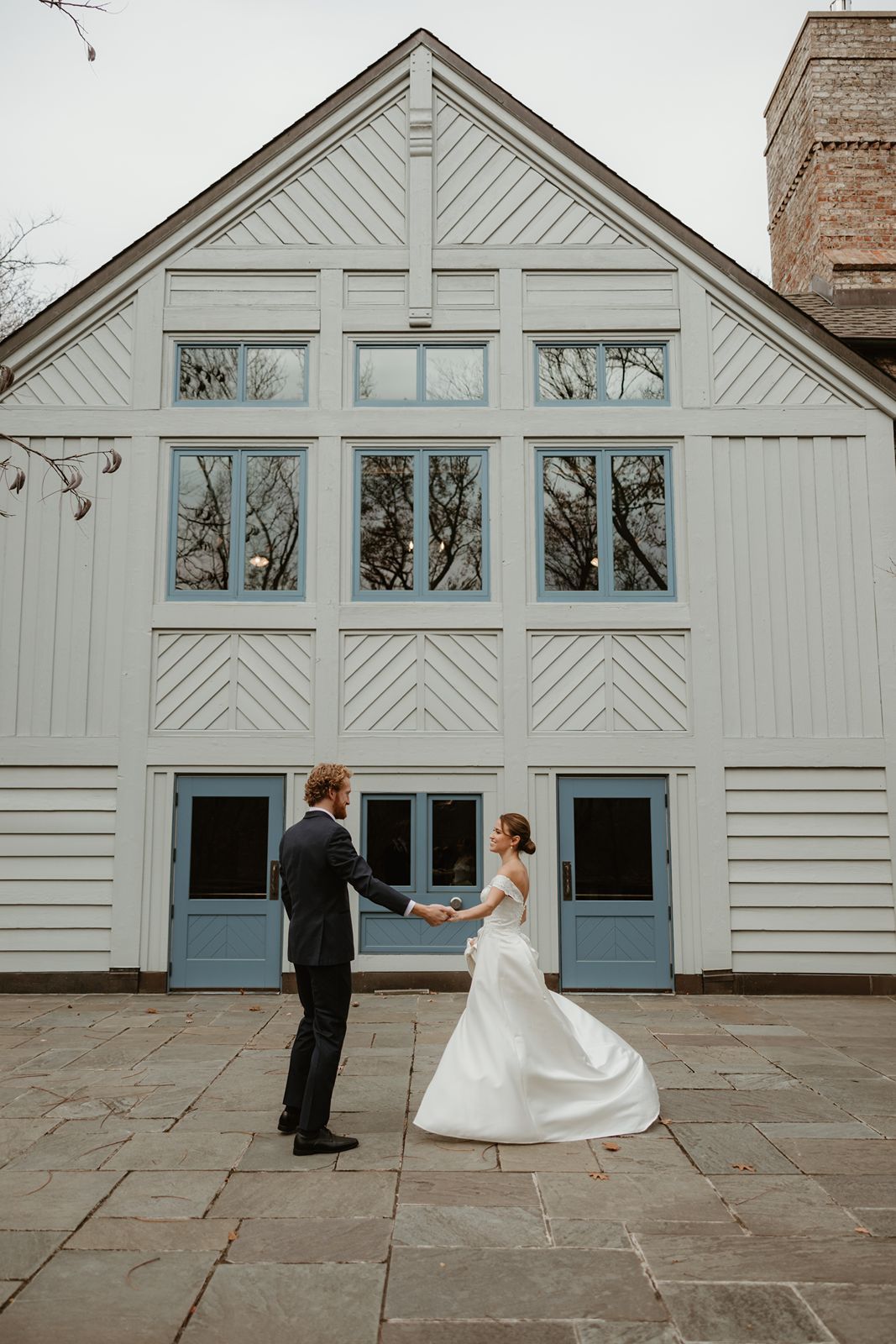 Couple dances in front of a white geometric building with blue doors during their wedding.