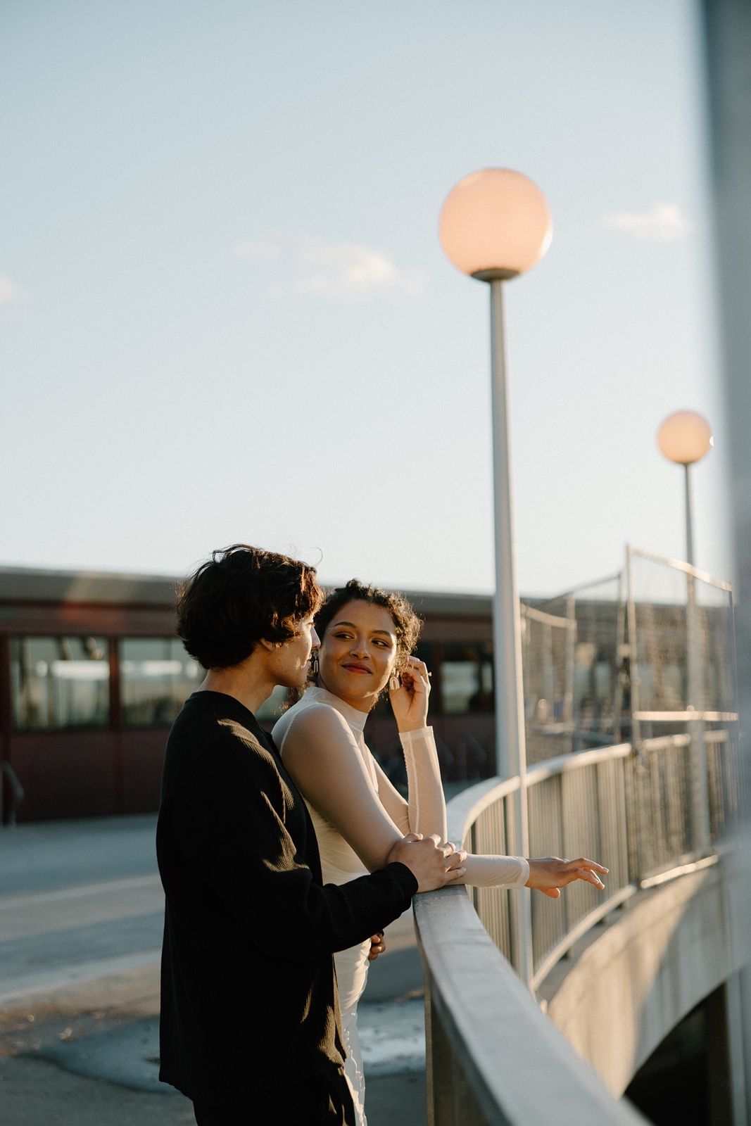 Couple standing by a railing at dusk with glowing street lamps and a clear sky in the background.