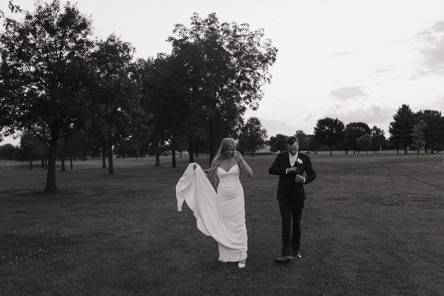 A black and white wedding photo series showing a couple posing together in an outdoor field with trees in the background.