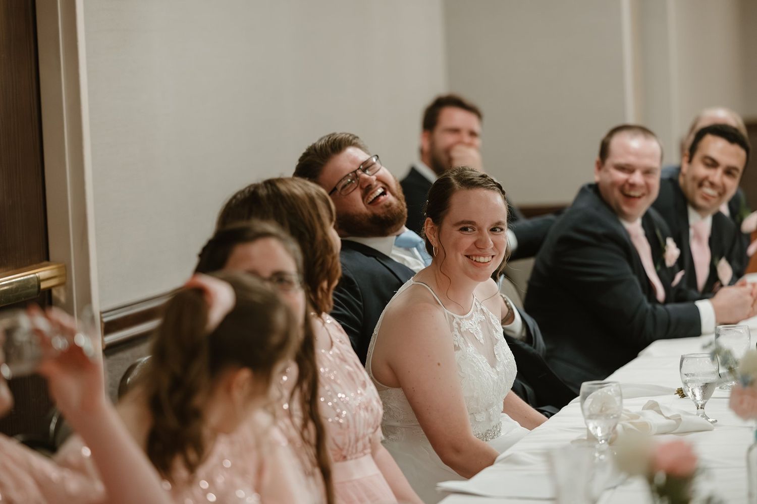 Wedding guests laugh and smile while seated at reception tables during a joyful celebration.