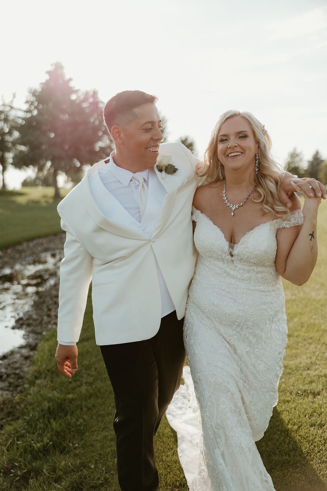 A joyful wedding couple walks together on a scenic golf course path.