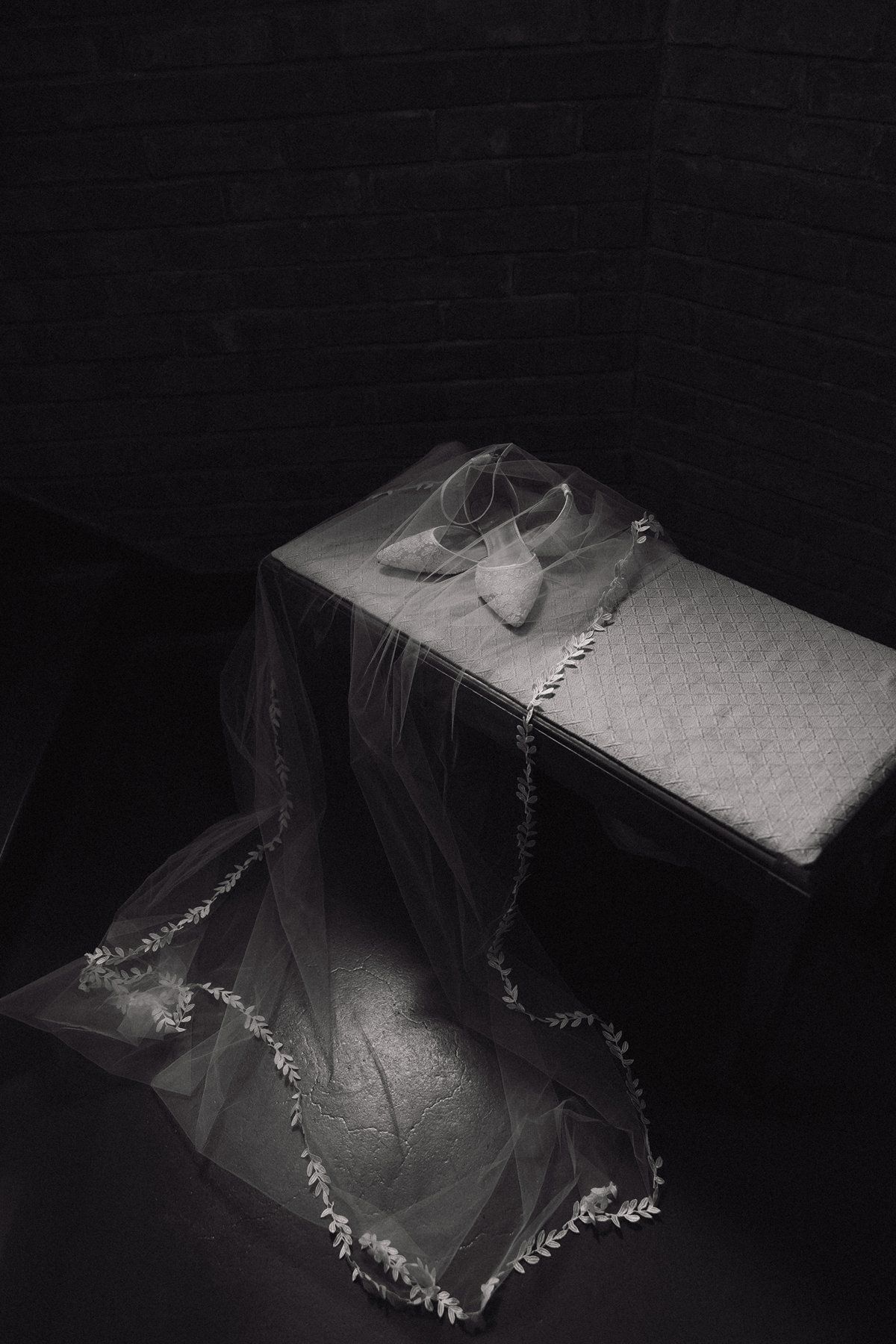 Black and white photograph shows intricate lace details of a wedding veil against a dark background.