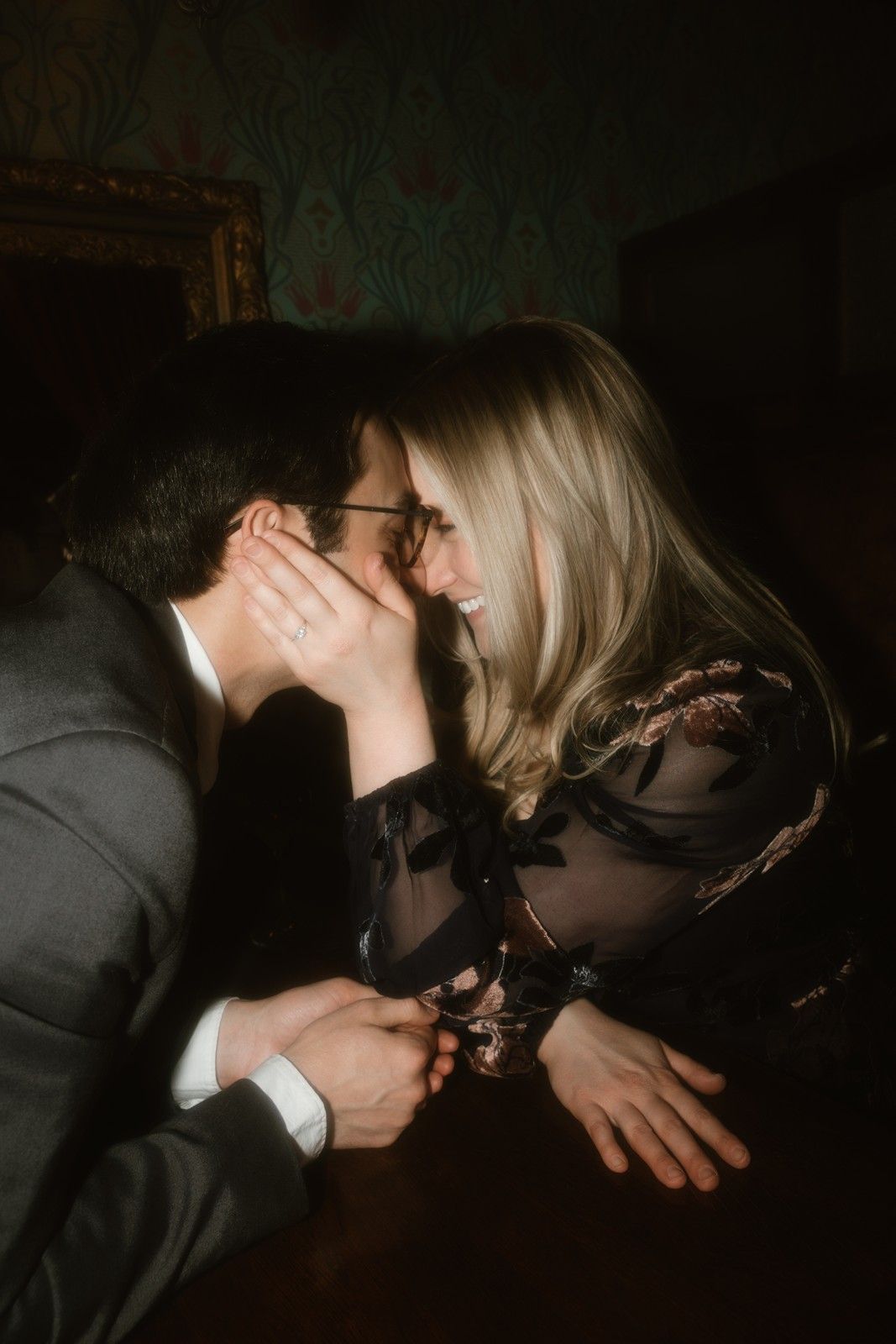 Couple sharing a close intimate whispered moment in dark moody lighting at vintage bar.