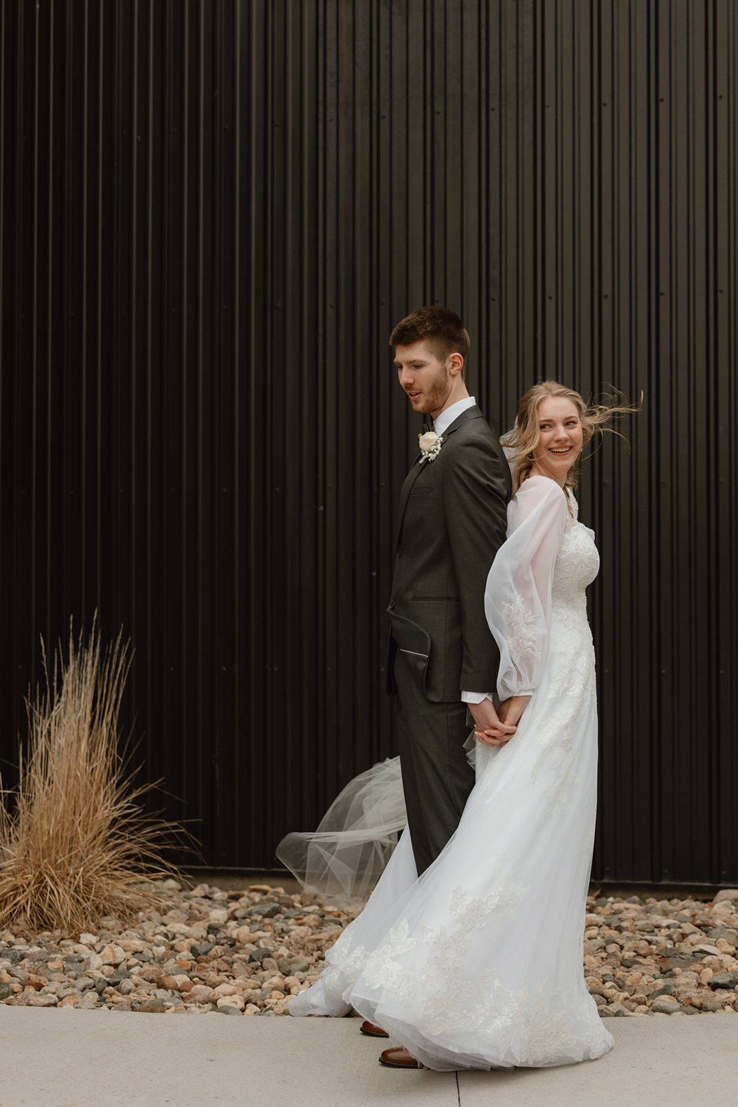 A couple in formal wedding attire poses against a dark wall with dried grass decor in a series of romantic shots.
